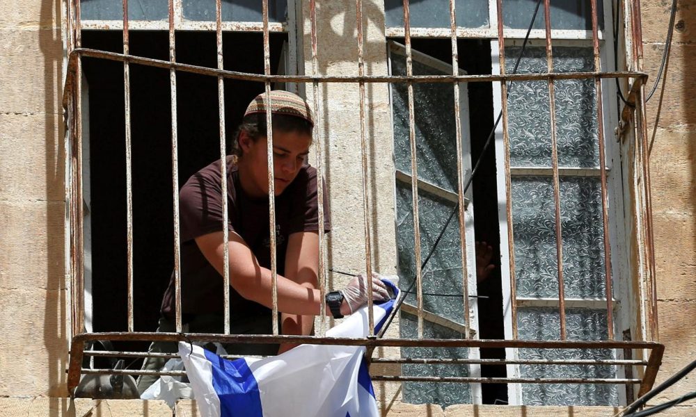 Imagen de archivo de un colono judío que cuelga una bandera israelí en una de las ventanas de un edificio palestino cerca de la mezquita de Ibrahimi, en la ciudad cisjordana de Hebrón. EFE/ Abed Al Hashlamoun