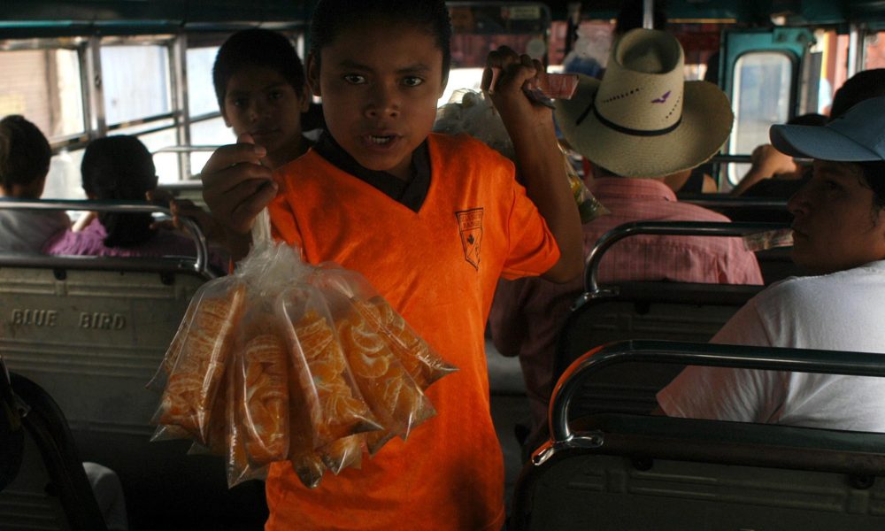 Fotografía de un niño al vender bolsas de mandarinas en un autobús en Tegucigalpa (Honduras). EFE/Gustavo Amador