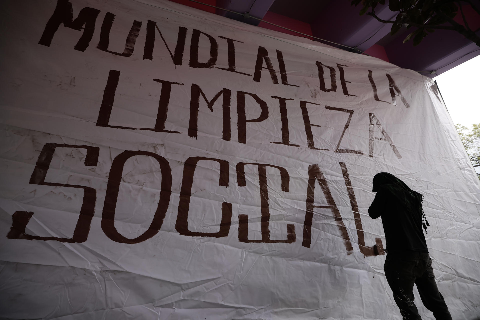 Un activista posa junto a un cartel durante una manifestación, donde acusan a las autoridades de intentar "borrar" sus demandas por el acceso al agua y la defensa del territorio, tras el retiro de un mural comunitario instalado en las inmediaciones del estadio Azteca, este martes en Ciudad de México (México). EFE/ José Méndez