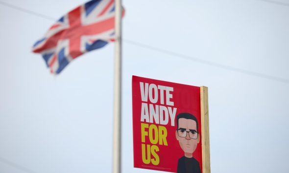 Una bandera del Reino Unido ondea cerca de un cartel del candidato laborista Andy Burnham en Wigan, Reino Unido, en una imagen del 15 de junio de 2026. La circunscripción inglesa de Makerfield celebra este jueves una elección parcial para elegir a su nuevo diputado, cita en la que Burnham concurre como candidato laborista a fin de entrar en el Parlamento y desafiar eventualmente el liderazgo de Keir Starmer. EFE/EPA/ADAM VAUGHAN