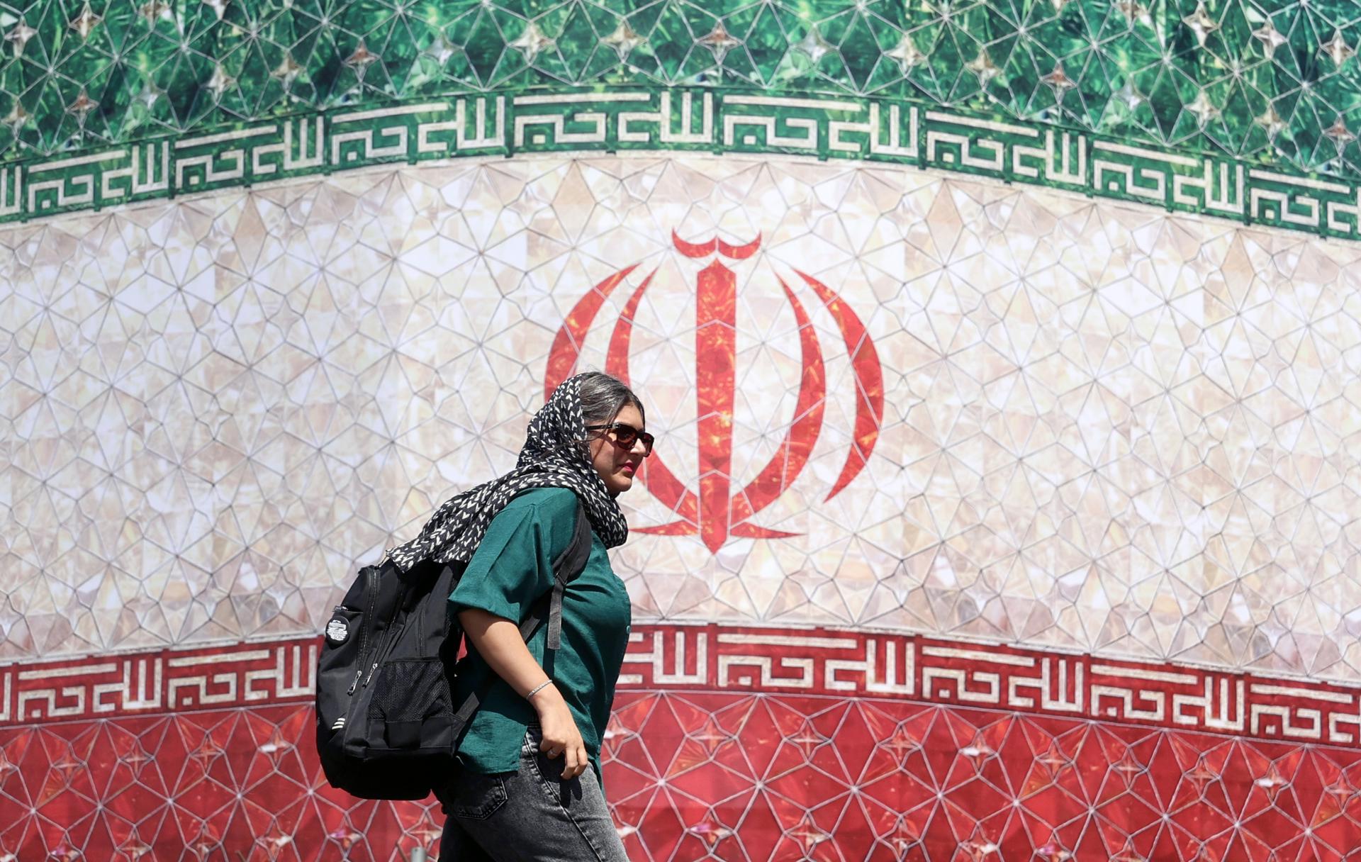 Una mujer iraní pasa junto a una valla publicitaria con la bandera nacional de Irán en la plaza Enqelab de Teherán, Irán. EFE/EPA/ABEDIN TAHERKENAREH. RESTRICCIONES: Prohibido el acceso a medios de comunicación israelíes/canales de televisión en persa fuera de Irán/Prohibido el acceso a BBC Persian/VOA Persian/Manoto TV/Televisión Internacional de Irán. (Según lo dispuesto por la Dirección General de Medios de Comunicación Extranjeros de Irán).