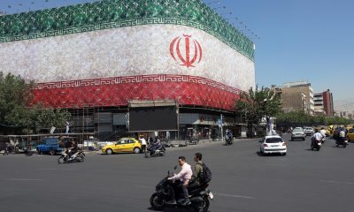 Unos iraníes pasan en coche junto a una valla publicitaria con la bandera nacional de Irán en la plaza Enqelab de Teherán, Irán. EFE/Abedin Taherkenareh