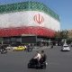 Unos iraníes pasan en coche junto a una valla publicitaria con la bandera nacional de Irán en la plaza Enqelab de Teherán, Irán. EFE/Abedin Taherkenareh